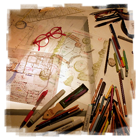 Der Blick auf den Schreibtisch von DI Paula Polak. Neben den in Arbeit befindlichen Skizzen liegen neben dem Geodreieck, einem Bleistift, Radierer und der roten Brille, auch zahlreiche Bunt- und Filzstifte.
